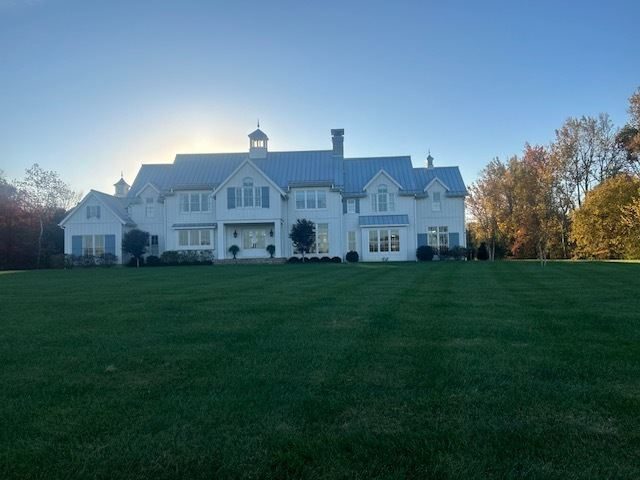 Large maintained lawn in front of a white farmhouse at sunset